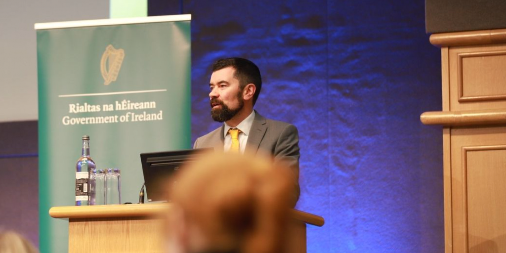 This article is about a video on inclusive decision-making for Irish communities. In the photo, Irish Minister of State Joe O’Brien, speaking to a crowd.