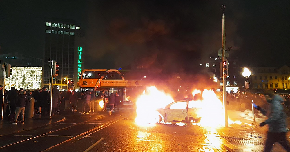 Photo of O'Connell bridge during the Dublin riots, with four men arrested in connection with the case. The image shows a group of people and a car on fire.