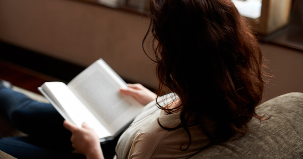 This article is about queer books to read in winter. In the photo, a persona reading a book on a sofa.