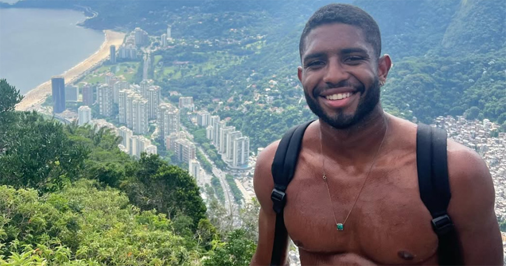 An image of Joao Lucas Reis Da Silva. He poses smiling, shirtless and with a scenic view in the background.