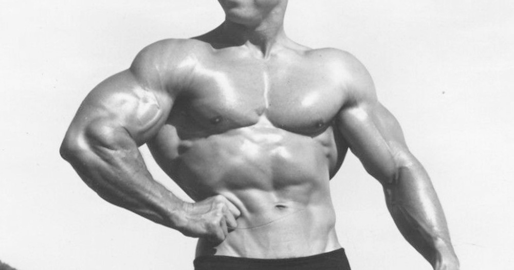 A black and white image of someone involved in bodybuilding. It shows their naked torso with flexed muscles.