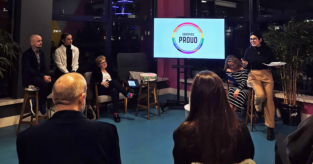 People attending a Certified Proud event for LGBTQ+ inclusion in the workplace. A panel of speakers faces the audience in a room.