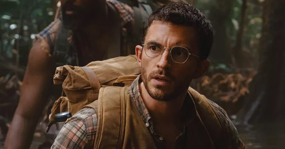 Jonathan Bailey playing a character in Jurassic World: Rebirth. He's dressed as a palaeontologist as he walks in the forest with another person in the background.