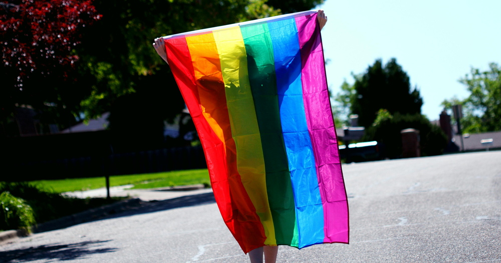 Person walking with the LGBTQ+ flag as opposed to queer impostor syndrome