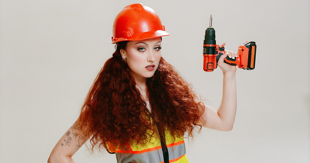 Image of 'The Giver' singer Chappell Roan wearing a construction worker outfit including a helmet, high vis jacket and a drill.