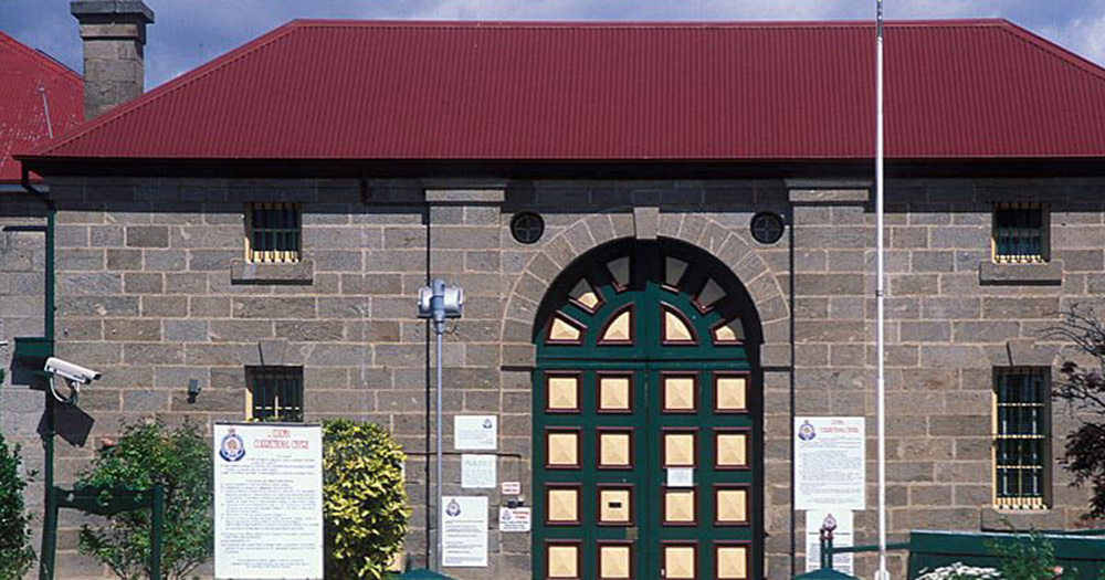 Australia's former gay prison, Cooma Gaol, a gray bricked building with green doors and a red roof.