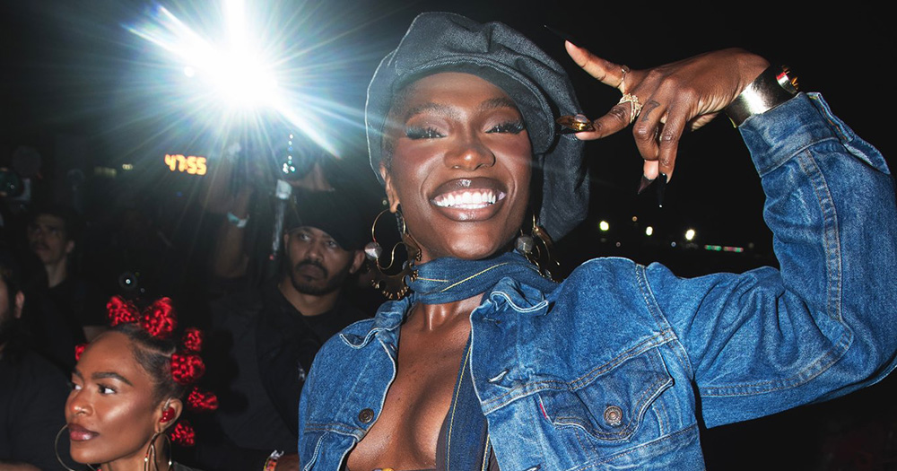 An image of Billboard Woman of the Year Doechii. She smiles and makes a peace sign with her fingers.