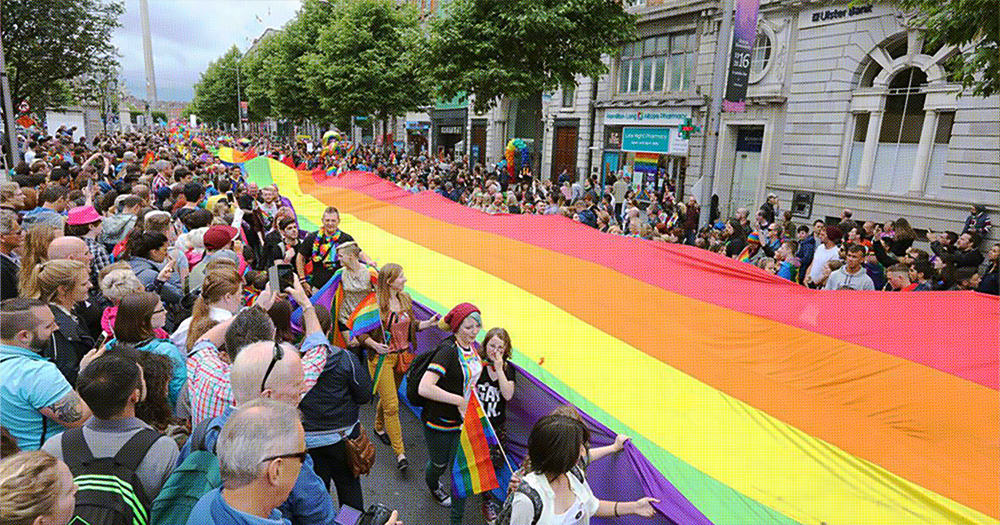 This article is about Dublin Pride 2025. In the photo, people marching in Pride and holding a long Pride flag.