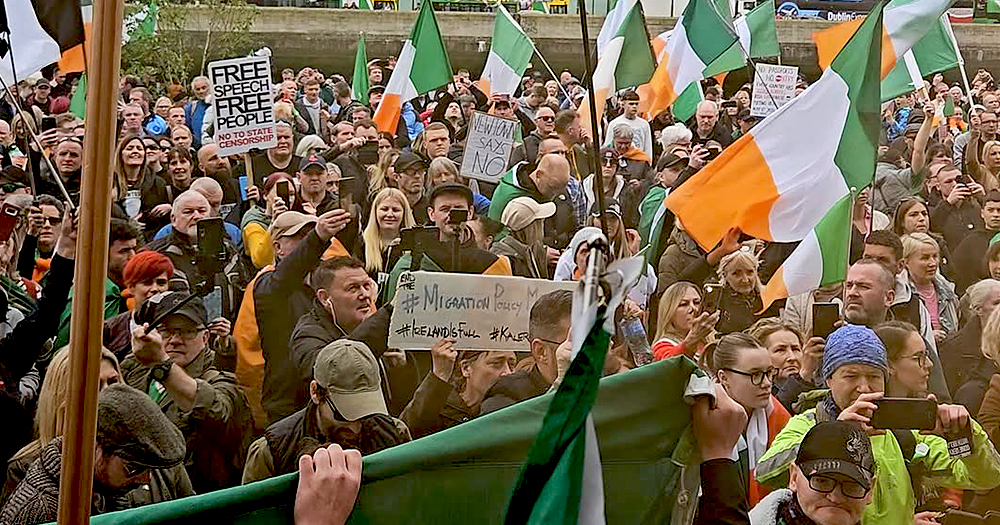 This article is about asylum seekers centres not opening because of violent protest and criminality. In the photo, people attending an anti-immigration protest in Dublin, waving Irish flags.