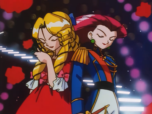 The villains of the anime Pokémon are standing on screen back to back while they are both crossdressing. The villian, James, is wear a red dress and a blonde wig with curls as Jessie is wearing a prince uniform