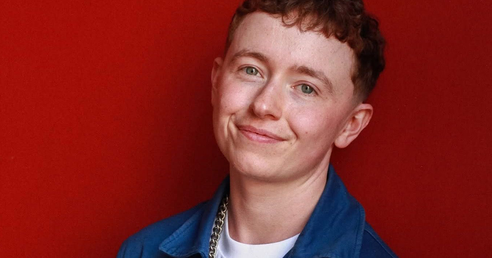 Activist Ruadhán Ó Críodáin, who has been announced as the 2025 Grand Marshall of Dublin Pride, smiling at the camera with a red background.