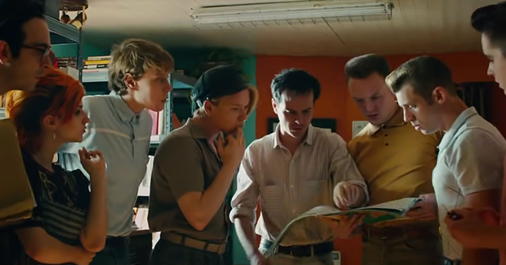 A screenshot from the Pride film, which is getting a musical adaptation. Left to right: Joe Gilgun, Faye Marsay, george mackay, Freddie Fox, Andrew Scott,Ben Schnetzer, are standing in a circle looking down at a book.