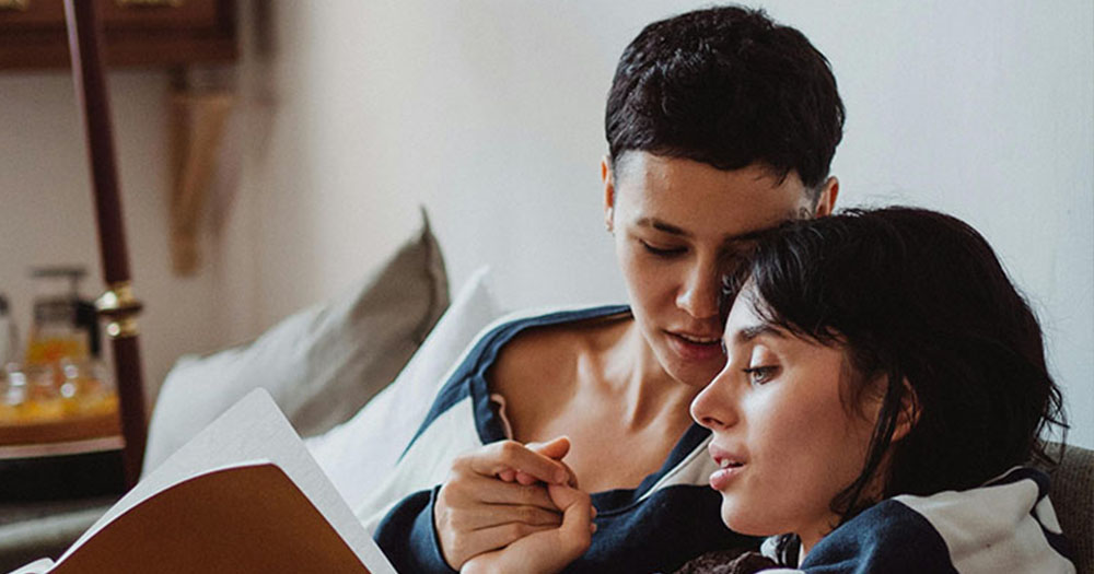 This article is about Hinge partnering with authors to tell real love stories. Two women cuddling and reading a book.