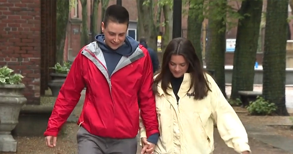 Ansley Baker wearing red jacket and hoodie and Liz Victor wearing a yellow jacket walking and holding hands. This is the couple that was kicked out of a Boston hotel.