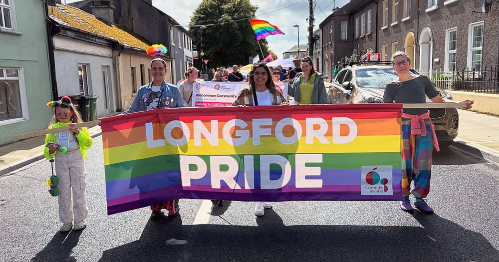Photo of participants of Longford Pride, coming back in 2025. Paricipants are walking down a street with a banner than reads "Longford Pride".