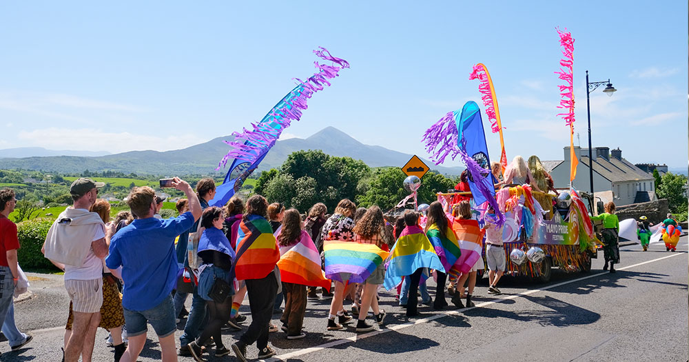 Mayo Pride parade in the sun with flags and banners.