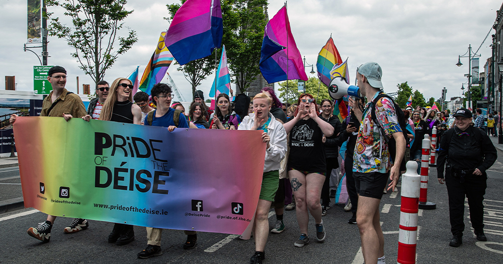 People talking part in Pride of the Déise, marching down a street carrying Pride flags and a colourful banner.