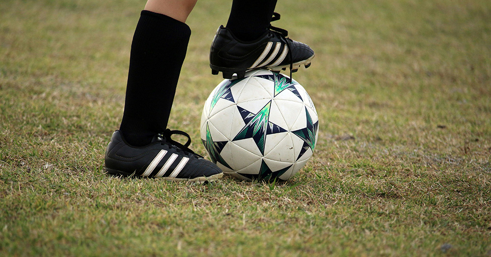 This article is about trans women playing football in Ireland. The image shows the lower half of someone's legs, with their right foot on top of a football.