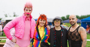 Four people standing together at Wexford Pride, a drag artist wearing all pink, a person with red hair wearing a rainbow suit, a person wearing a blazer, cap and headphones and person wearing dark make-up and lacy shirt.