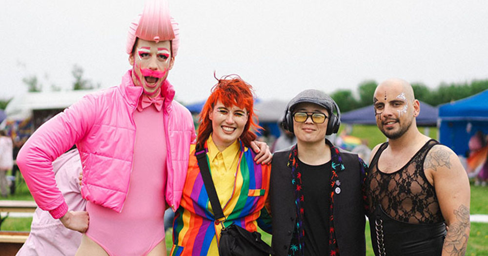 Four people standing together at Wexford Pride, a drag artist wearing all pink, a person with red hair wearing a rainbow suit, a person wearing a blazer, cap and headphones and person wearing dark make-up and lacy shirt.