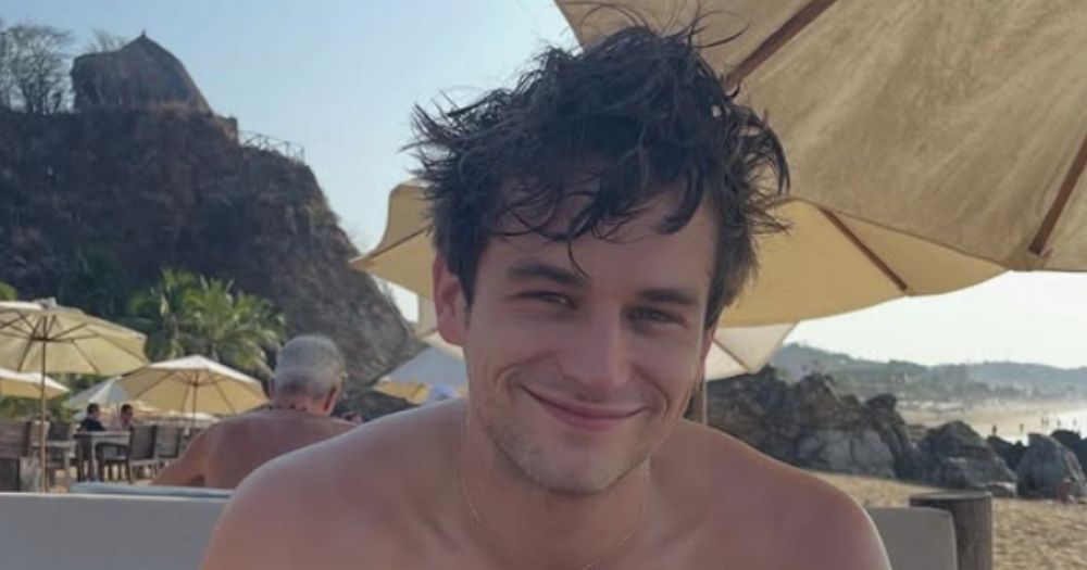 Brandon Flynn smiling at the camera sitting outside at the beach