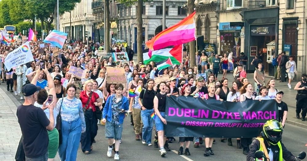 Crowd attending the Dyke March in Dublin, walking down O'Connell Street carrying banners and flags.