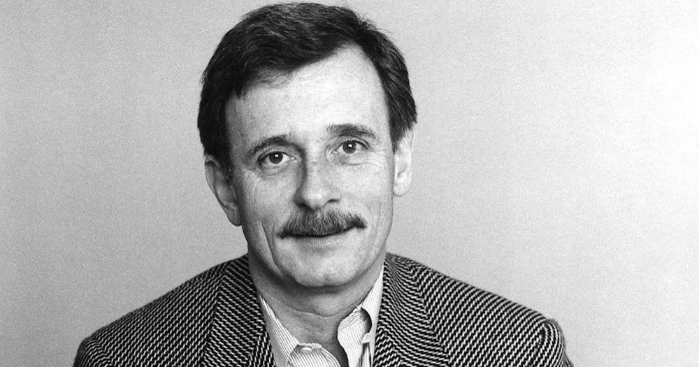 Writer Edmund White smiling at the camera in a black and white photo.