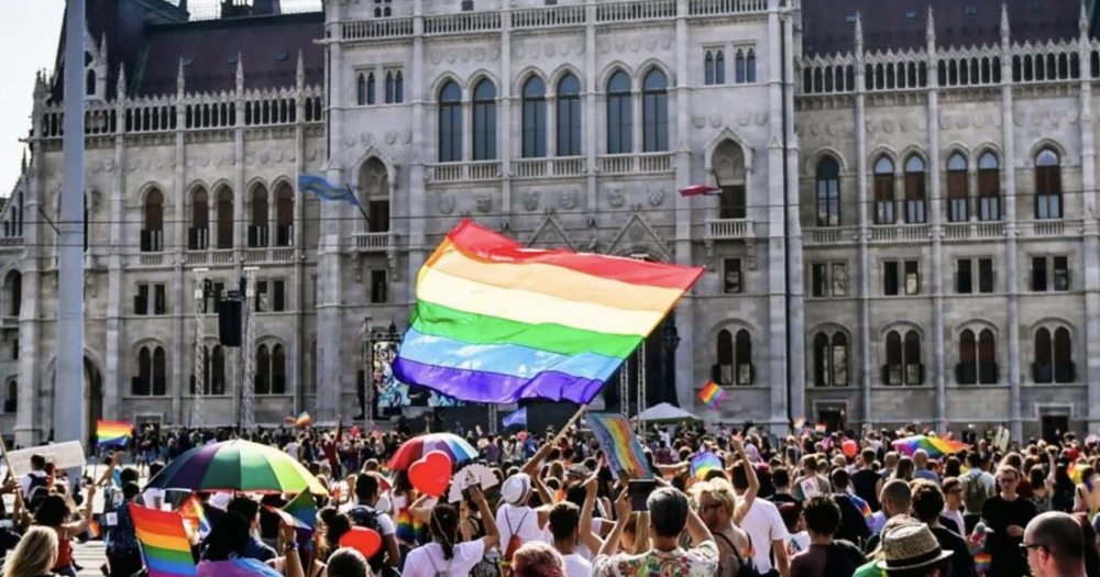 This article is about EU inaction on Hungary's crackdown on LGBTQ+ rights. In the photo, people marching in a Pride parade with a big Pride flag.