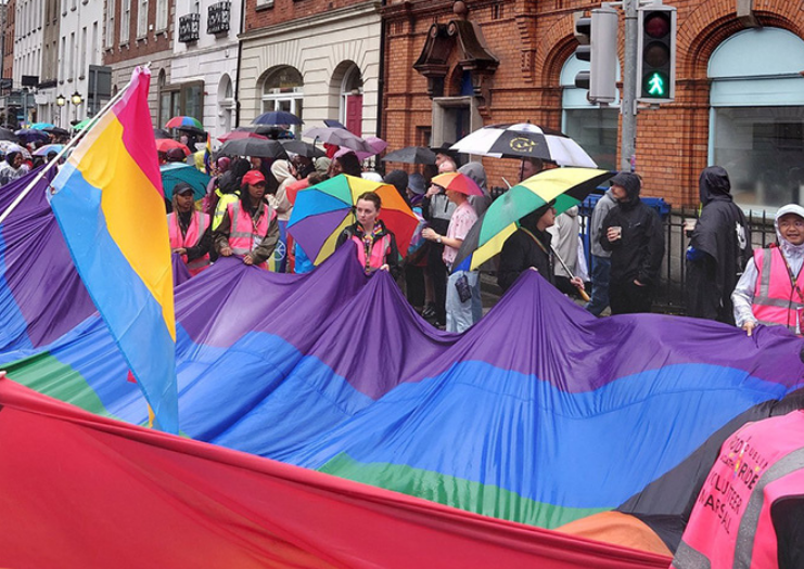 Photos of participants walking down the street with a massive rainbow flag at a rainy 2024 Dublin Pride Parade.