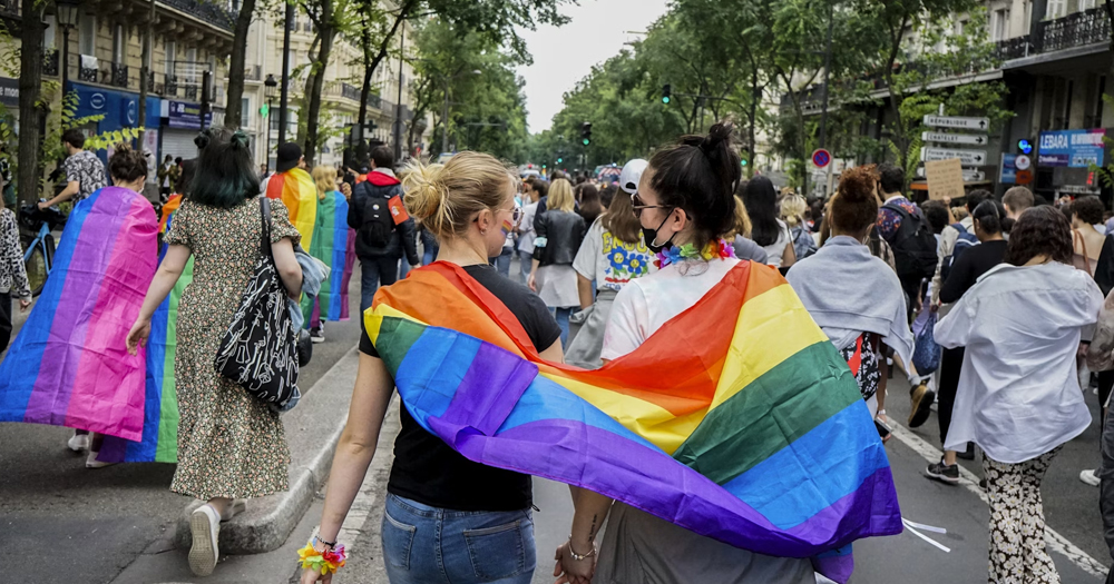 This article is about the MyLife Pride 10 Day Challenge. In the photo, two people hugging each other while walkin in a parade, with a Pride flag on their shoulders.