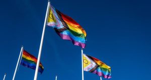 This article is about LGBTQ+ people reporting discrimination in Ireland. In the photo, some progress Pride flags flowing in a blue sky.
