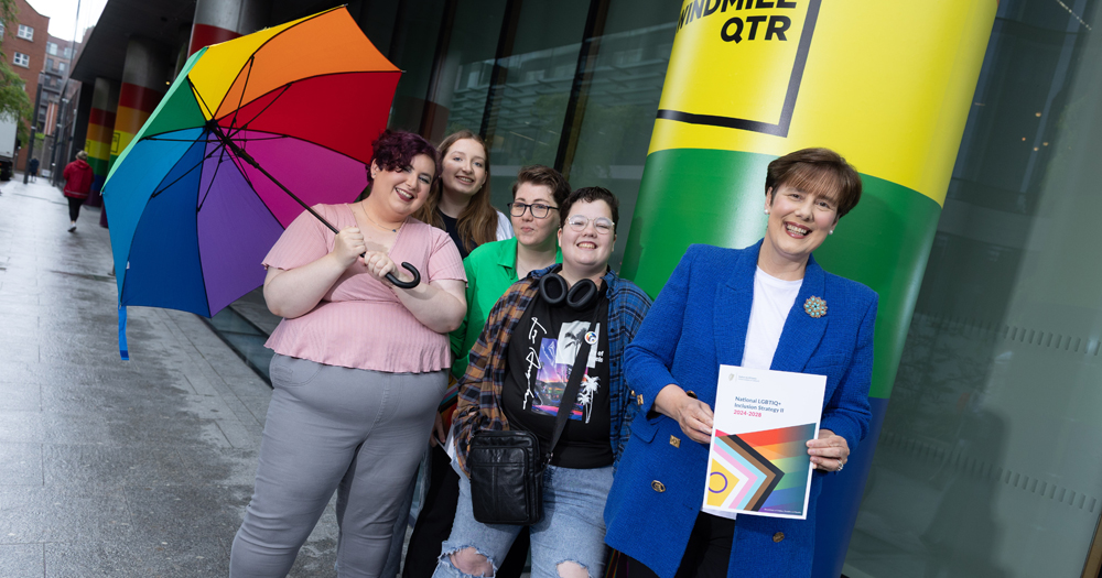 Minister Norma Foley holding the new LGBTQ+ inclusion strategy while posing for a picture with LGBTQ+ young people.