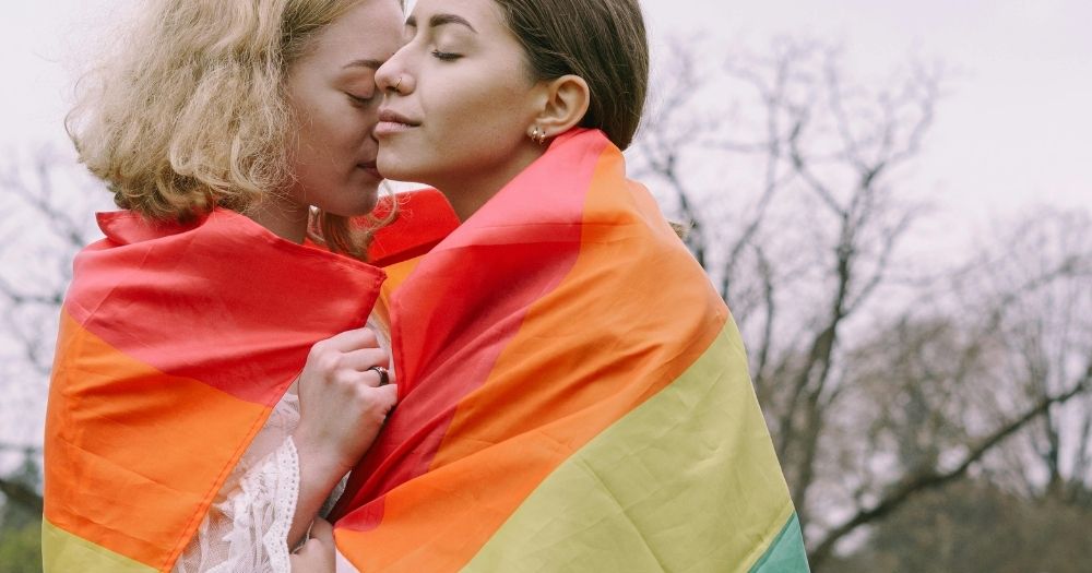 A same-sex couple embraced outside with a Pride flag wrapped around their shoulders.