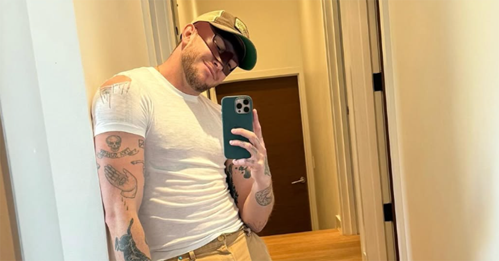 Street Fighter star Orville Peck taking a mirror selfie. He wears a white t-shirt, eye mask and cap.
