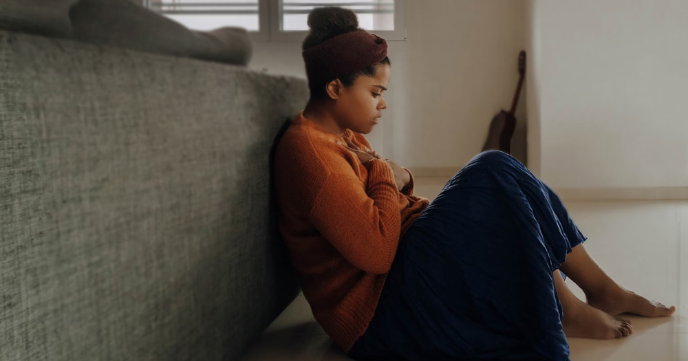 This article is about a podcast episode about intimate partner abuse in queer relationships. In the photo, a woman sitting on the floor with a worried expression on her face.