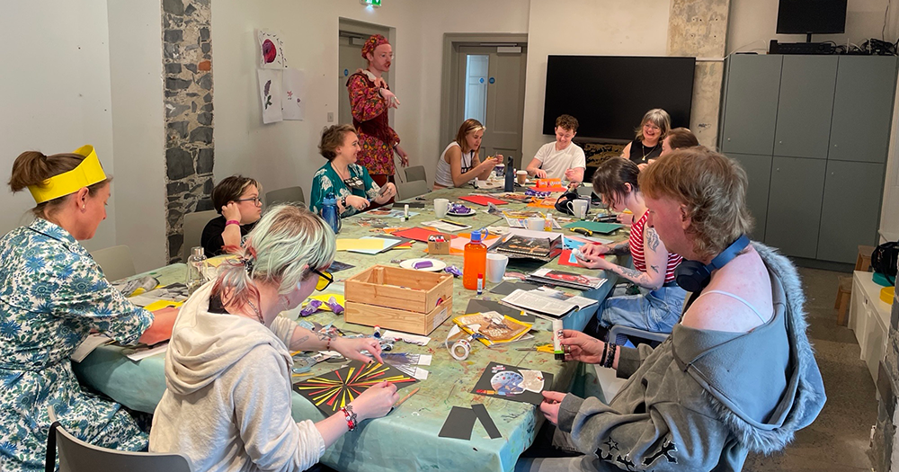 An image from the queer art club in Kilkenny. People sit around a table doing arts and crafts.