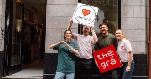 Four people standing in front of apparel shop The Grá, holding up signs with the name of the store.