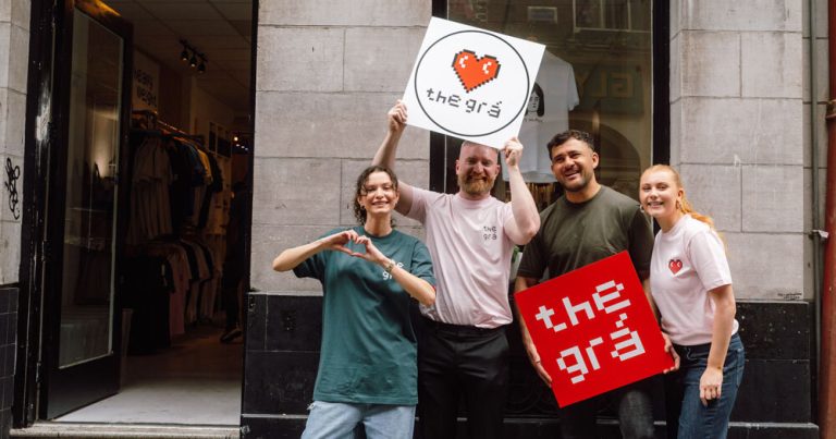 Four people standing in front of apparel shop The Grá, holding up signs with the name of the store.