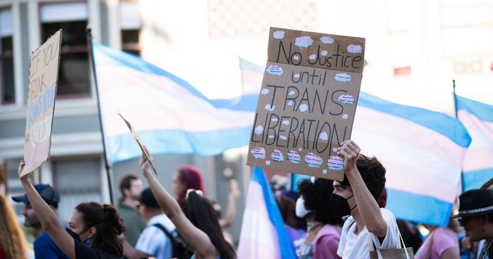 This article is about trans-inclusive lesbian activism. In the photo, a person carrying a sign that reads "No justice until trans liberation", with other people carrying trans flags.