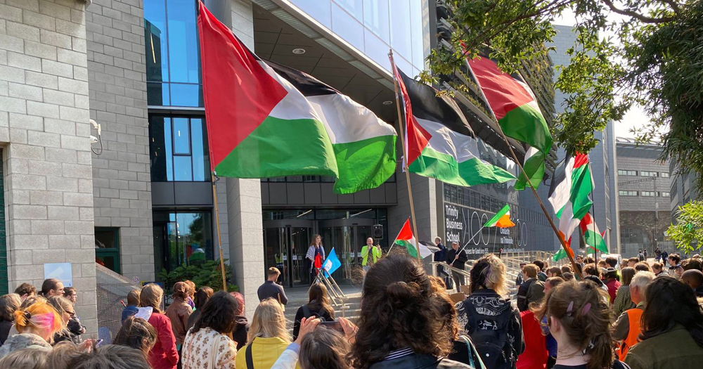 People protesting outside Trinity College calling for divestment from Israeli universities and companies, carrying Palestinian flags.
