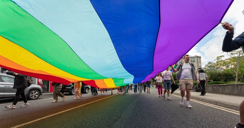 Photo of last year's Letterkenny Pride festival where people where holding a large Pride flag while marching.