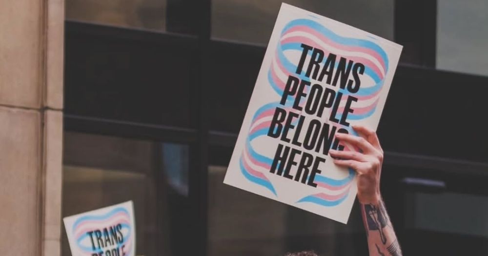 This article is about the first day people were able to apply for gender recognition in Ireland. In the photo, a hand holding up a sign that reads "Trans people belong here".