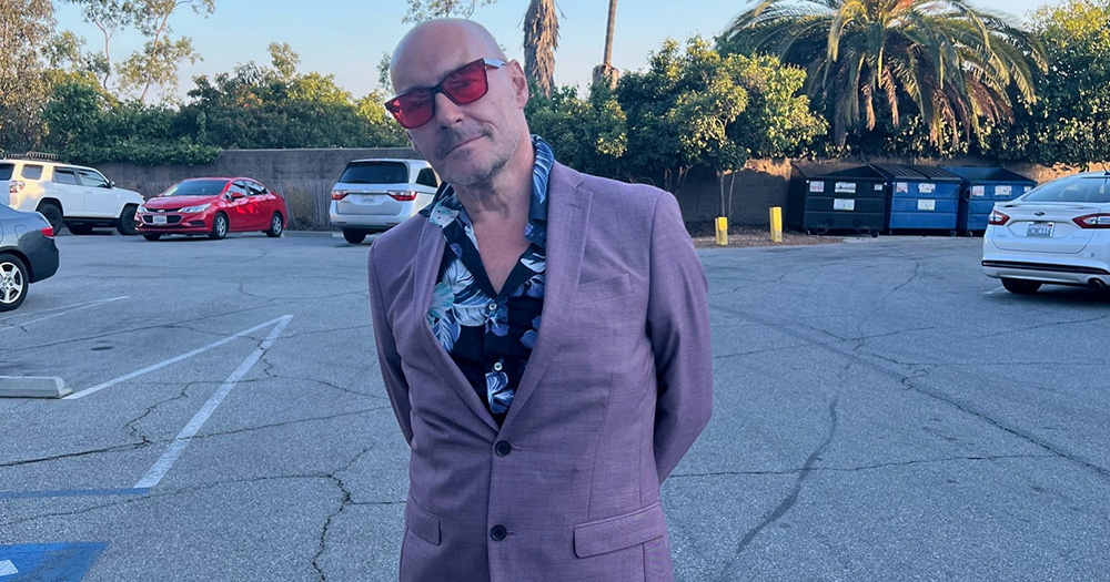 Grant Morrison posing for a photo in a suit.