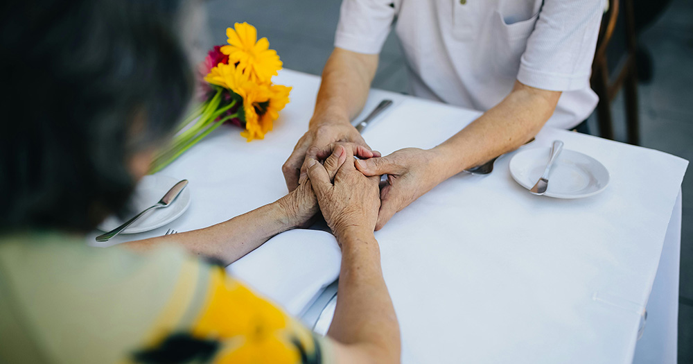 This article is about inheritance tax. The image shows the torsos of two older people sitting at a table and holding hands.
