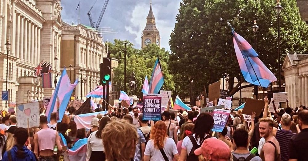 People marching at London Trans Pride, carrying trans flags and signs with slogans.