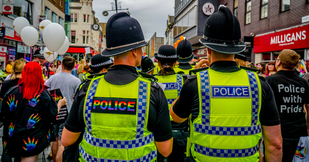 Police marching in Pride in the UK, which yellow vests that read "police" in the colours of the Pride flag.