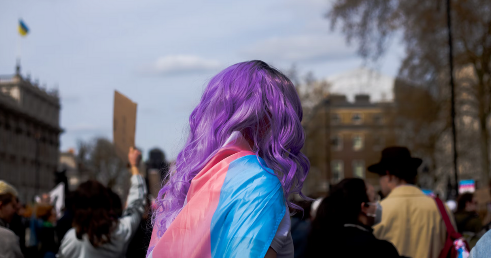 Image shows a person wearing trans flag - mirroring the theme of the piece covering a new report on trans lives after the UK Supreme Court ruling