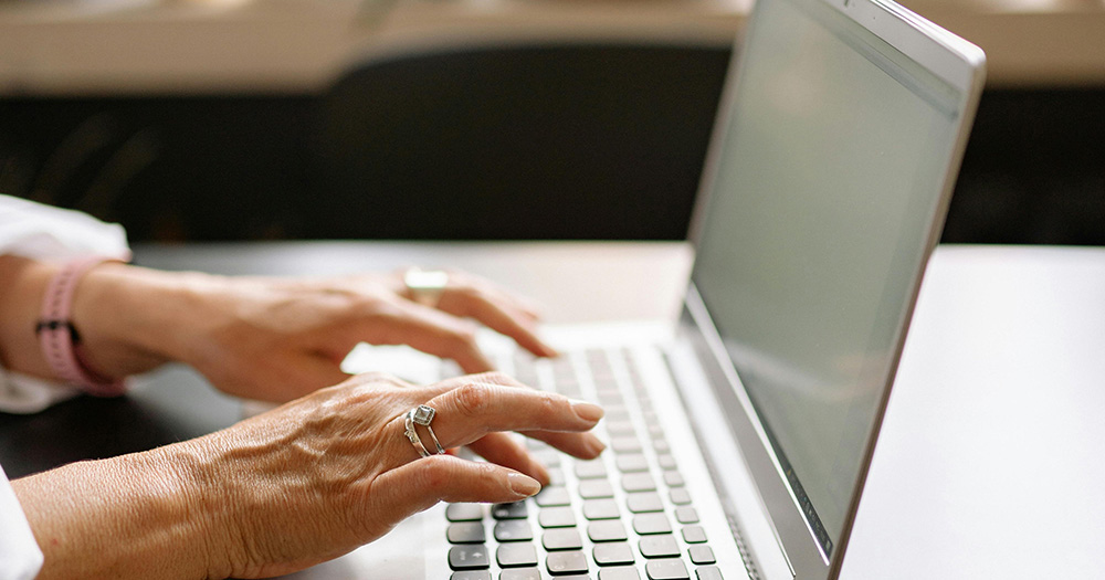 GCN is hiring for a temporary editor. The image shows hands typing on a laptop.