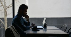 This article is about homophobia at work. The image shows a person sitting alone at a desk with a laptop in the dark.