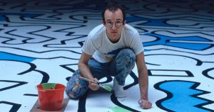 Keith Haring crouching down and painting on the floor.